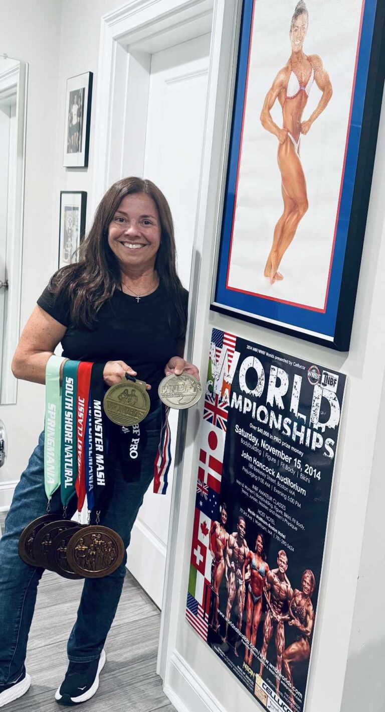 Nancy Andrews posing with medals from her natural bodybuilding events alongside a framed photo from her competitive career